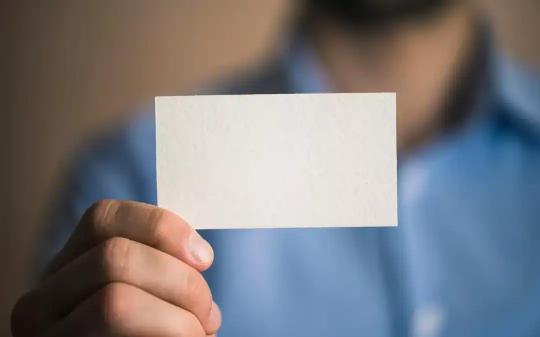 A blurry person in a blue shirt holds up a blank white business card.