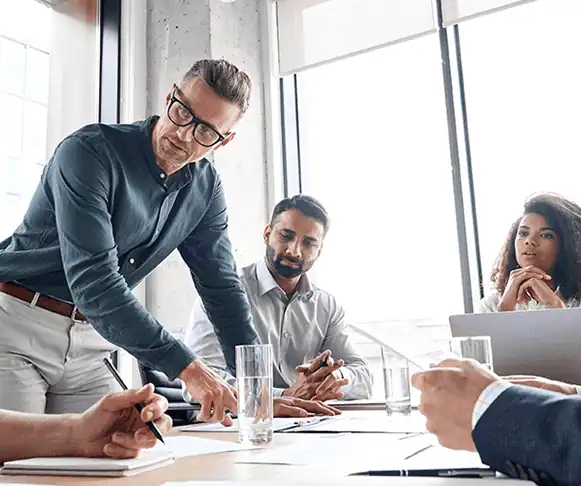 Group of diverse colleagues smiling and collaborating over documents on a desk during a team meeting in an office.